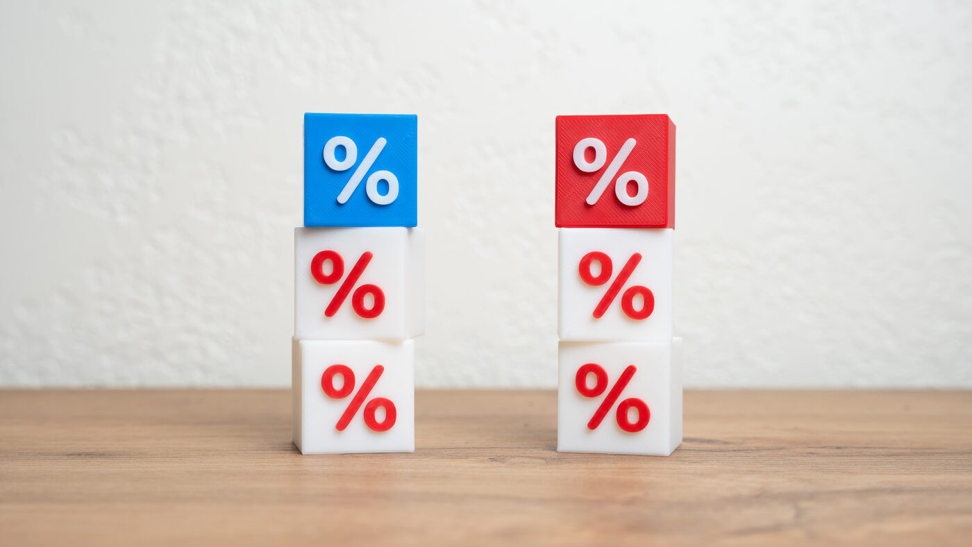 Two stacks of white blocks printed with percent signs on a wooden table, one topped with a blue block and the other with a red one